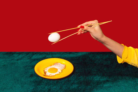 Womans hand tasting fried eggs with chopsticks isolated on green and red background. Vintage, retro style interior. Food pop art photography.の写真素材