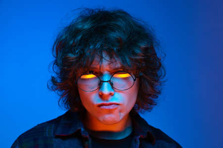 Close-up face of sad man, student looking at camera isolated on blue background in neon light....