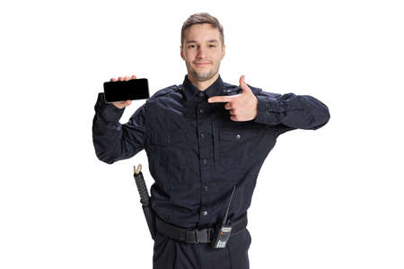 Portrait of young man, policeman officer wearing black uniform using phone isolated on white background. Concept of job, caree, law and order.の写真素材
