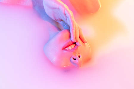 Closeup female face, young beautiful girl in milk bath with soft glow in blue-green neon light....