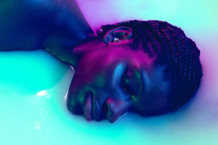 Profile view of female face of african girl in milk bath with soft white glowi in neon light. Modern...