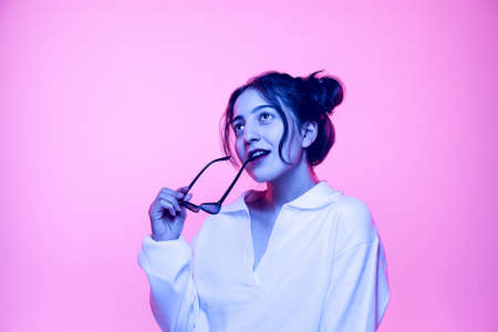 Half-length portrait of young beautiful girl in white blouse posing isolated on pink background in neon light. Concept of emotionsの写真素材