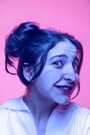 Close-up face of cute young girl crushed on glass isolated on light pink studio background in neon....