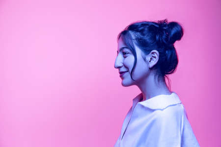 Half-length portrait of young beautiful girl in white blouse posing isolated on pink background in neon light. Concept of emotionsの写真素材