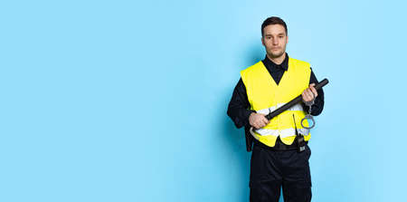 Half-length portrait of young male policeman officer wearing black uniform and warnvest posing isolated on blue background.の写真素材