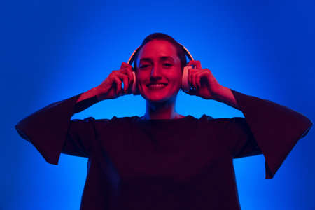 Happy pretty girl, student with short hair in black sweater in headphones isolated on dark blue...