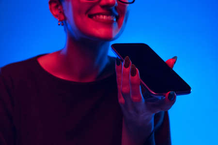 Cropped image of emotional young girl with hairdo buzzcut using phone isolated on dark blue...