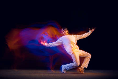 Dynamic portrait of male hip-hop dancer dancing isolated on dark background in mixed neon light....