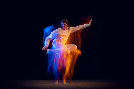 Dynamic portrait of male hip-hop dancer dancing isolated on dark background in mixed neon light....