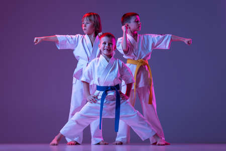 Three sportive kids, little boys, taekwondo or karate athletes in doboks posing isolated on very peri color background in neon. Concept of sport, martial artsの写真素材