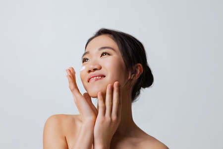 Cropped portrait of young beautiful woman doing skincare routine, moisturizing face with special creamの写真素材