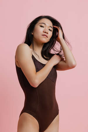 Portrait of tender young woman in brown bodysuit posing isolated over pink studio backgroundの写真素材