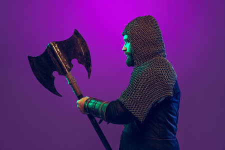 Studio shot of young bearded man in image of medieval warrior, archery in chain armor with ax...