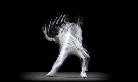 Young man, hip-hop dancer in action, motion isolated on dark background with sroboscope effect....