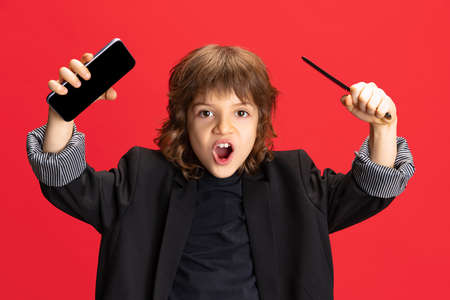 Emotional liitle cute boy, kid in image of stylish hairdresser, barber isolated on red background....