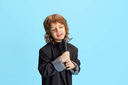 Studio shot of liitle cute boy, kid in image of stylish hairdresser, barber isolated on blue...