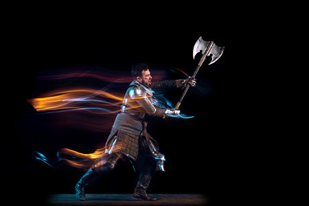 Dynamic portrait of brutal serious man, medieval knight with swinging ax fighting isolated over dark background in neon mixed light. Art, history, creativityの写真素材
