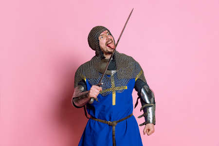 Portrait of man, medieval warrior or knight in armor with sword isolated over pink studio backgroundの写真素材