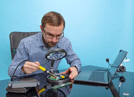 Potrait of professional programmer, technical specialist working with motherboard isolated over blue backgroundの写真素材