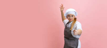 Comic portrait of lady-cook, chef in white hat and kitchen apron isolated on pink background....