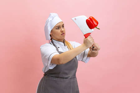 Comic portrait of lady-cook, chef in white hat and kitchen apron isolated on pink background....