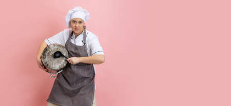 Comic portrait of lady-cook, chef in white hat and kitchen apron isolated on pink background. Cuisine, profession, business, food, taste, restaurant concept.の写真素材
