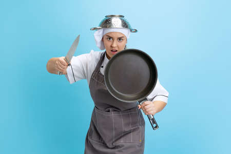 Kitchen knight. Comic portrait of pretty man, cook, female chef in white uniform having fun isolated on blue background. Funny meme emotions concept.の写真素材