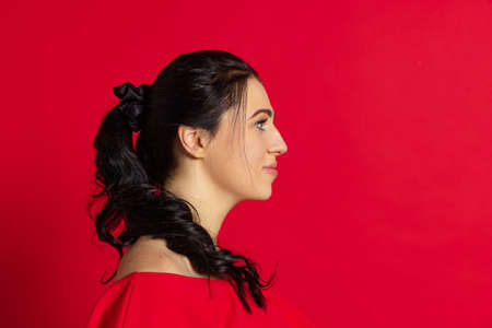 Profile view. Happy young beautiful girl with long glossy dark hair isolated on red background. Concept of emotions, facial expressionの写真素材