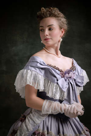 Vintage portrait of young adorable girl in image of medieval royal person in renaissance style dress isolated on dark background. Comparison of erasの写真素材