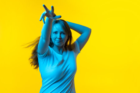 Beautiful young girl with freckles on her face dancing isolated on yellow background in neon. Concept of wow emotions, facial expressions, ad, salesの写真素材