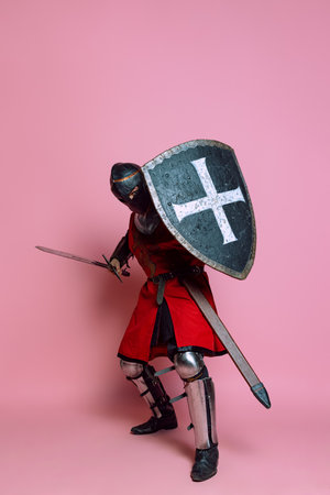 Portrait of medieval warrior or knight wearing armor clothing holding shield and sword isolated over pink background. Comparison of eras, historyの写真素材