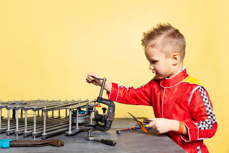 Cute little boy, child in image of auto mechanic or fitter in dungarees with work tools repairing auto motor isolated on yellow background.の写真素材