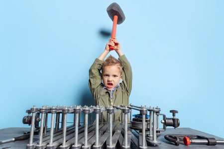 Comic portrait of preschool boy, kid in image of auto mechanic or fitter in dungarees with work tools having fun isolated on blue background.の写真素材
