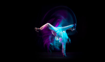 One energy young flexible sportive man dancing hip-hop or breakdance in white outfit on dark...