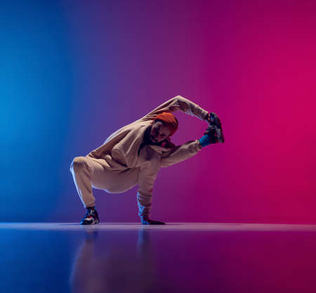 Studio shot of young flexible sportive man dancing breakdance in white outfit on gradient pink blue background. Concept of action, art, beauty, sport, youthの写真素材