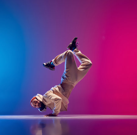 Free fall. Studio shot of young flexible sportive man dancing breakdance in white outfit on gradient...