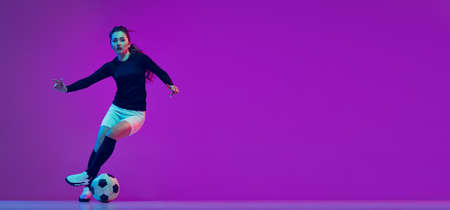 Professional female soccer player dribbling football ball isolated on purple studio background in neon light. Sport, action, motion, fitnessの写真素材