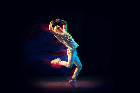 Freedom. Flexible man in white jeans and tee dancing hip-hop isolated on dark background in mixed...