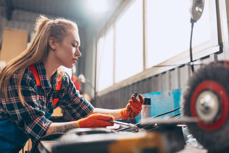 Female auto mechanic. beautiful young red-headed girl in working process at auto service station, indoors. Gender equality. Work, occupation, fashion, jobの写真素材