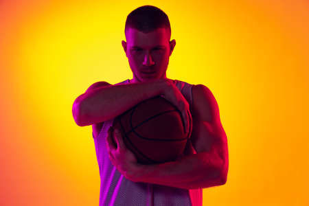Studio shot of muscled man, basketball player, danker isolated on gradient yellow purple background...