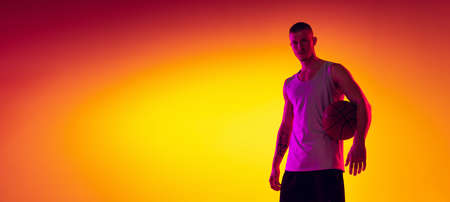 Studio shot of muscled man, basketball player, danker isolated on gradient yellow purple background in neon light. Beauty, sport, motion, activity concepts.の写真素材