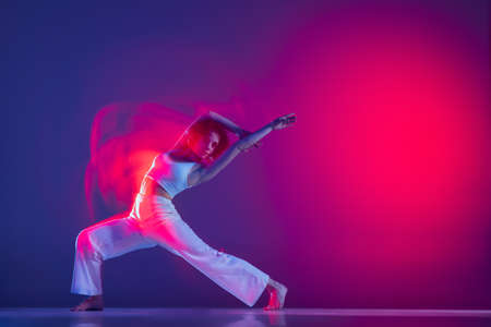 Young sportive beautiful girl, hip-hop dancer dancing hip hop isolated on purple background in pink neon light. Youth culture, style and fashion, action.の写真素材