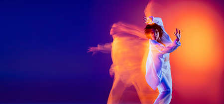 Image of flexible young girl, hip-hop dancer in white outfit dancing hip hop isolated on blue...