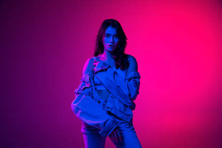 Beautiful young emotional girl, student with long dark hair isolated on gradient pink-blue background in neon light. Concept of emotions, youthの写真素材