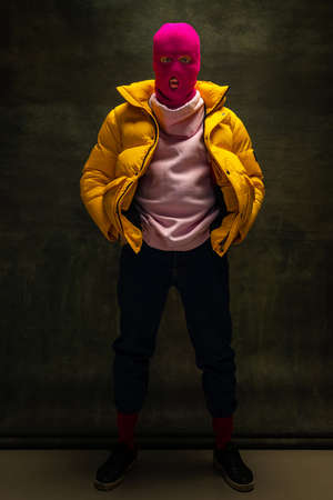 Studio shot of young anonymous man wearing pink balaclava and yellow down jacket, coat isolated on...