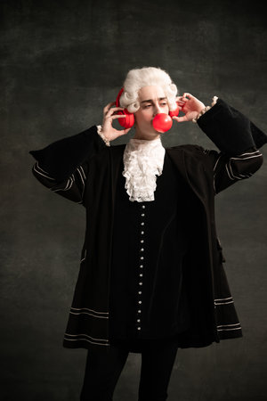 Portrait of young man wearing wig and vintage medieval outfit like famous composer having fun...