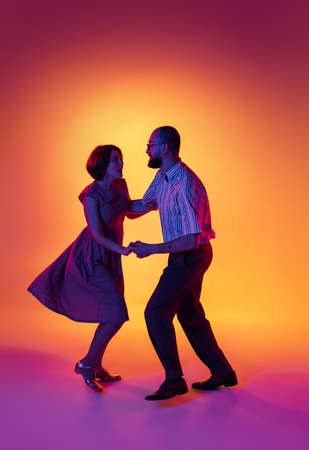 Portrait of excited man and woman, couple of dancers in vintage retro style outfits dancing lindy hop dance isolated on gradient yellow and purple background.の写真素材