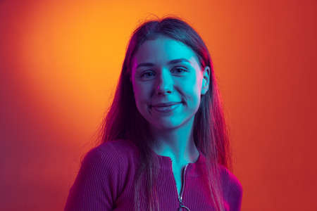 Closeup young beautiful girl looking at camera and smiling isolated on orange background in neon light, filter. Concept of emotionsの写真素材