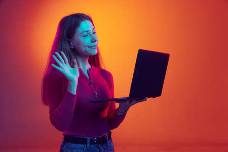 One emotional young beautiful using laptop isolated on orange background in neon light, filter....