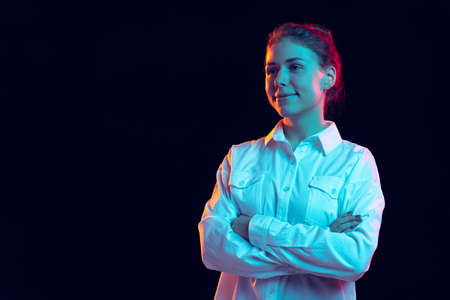 Half-length portrait of young pretty girl in white shirt isolated on dark background in blue neon light, filter. Concept of emotions, fashion, youthの写真素材